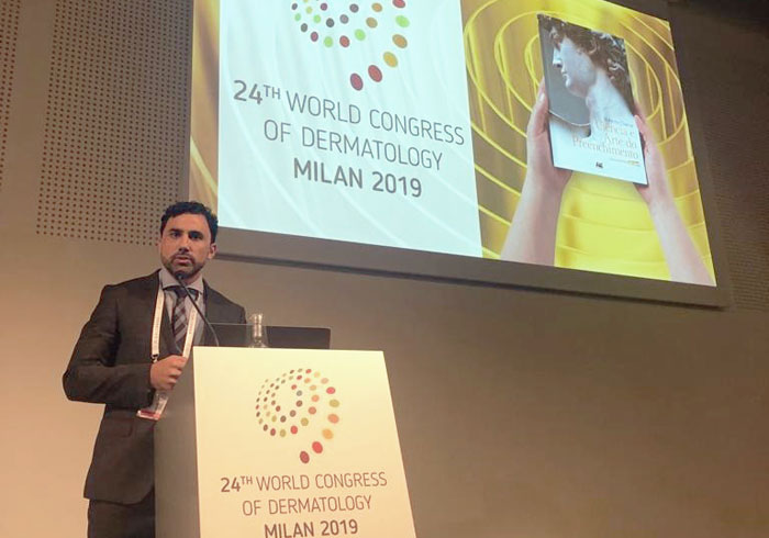 dr roberto chacur no palco com microfone e o primeiro slide de sua apresentação no congresso mundial de medicina 2019 na itália atrás